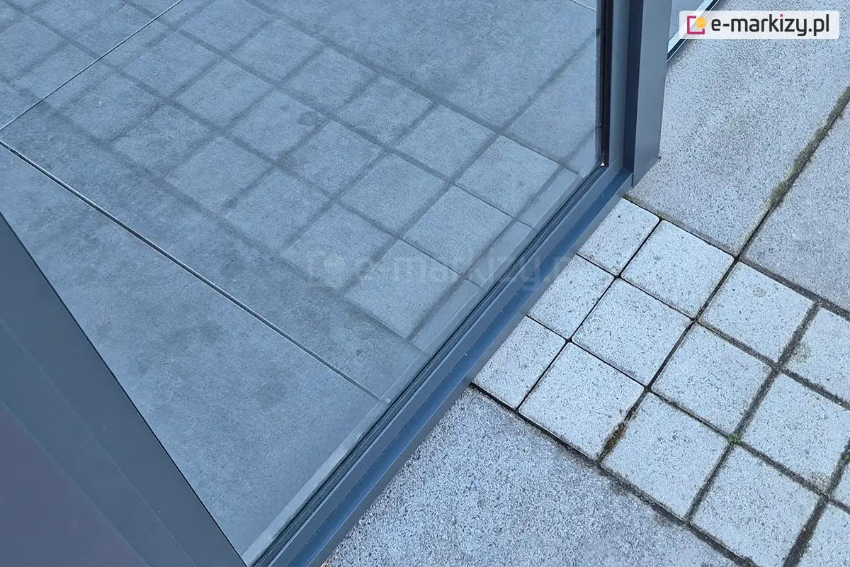 Nowoczesna stała witryna szklana systemu Fest z aluminiową ramą, elegancko osadzona na tarasie z płytkami, idealna do zabudowy tarasowej lub ogrodowej