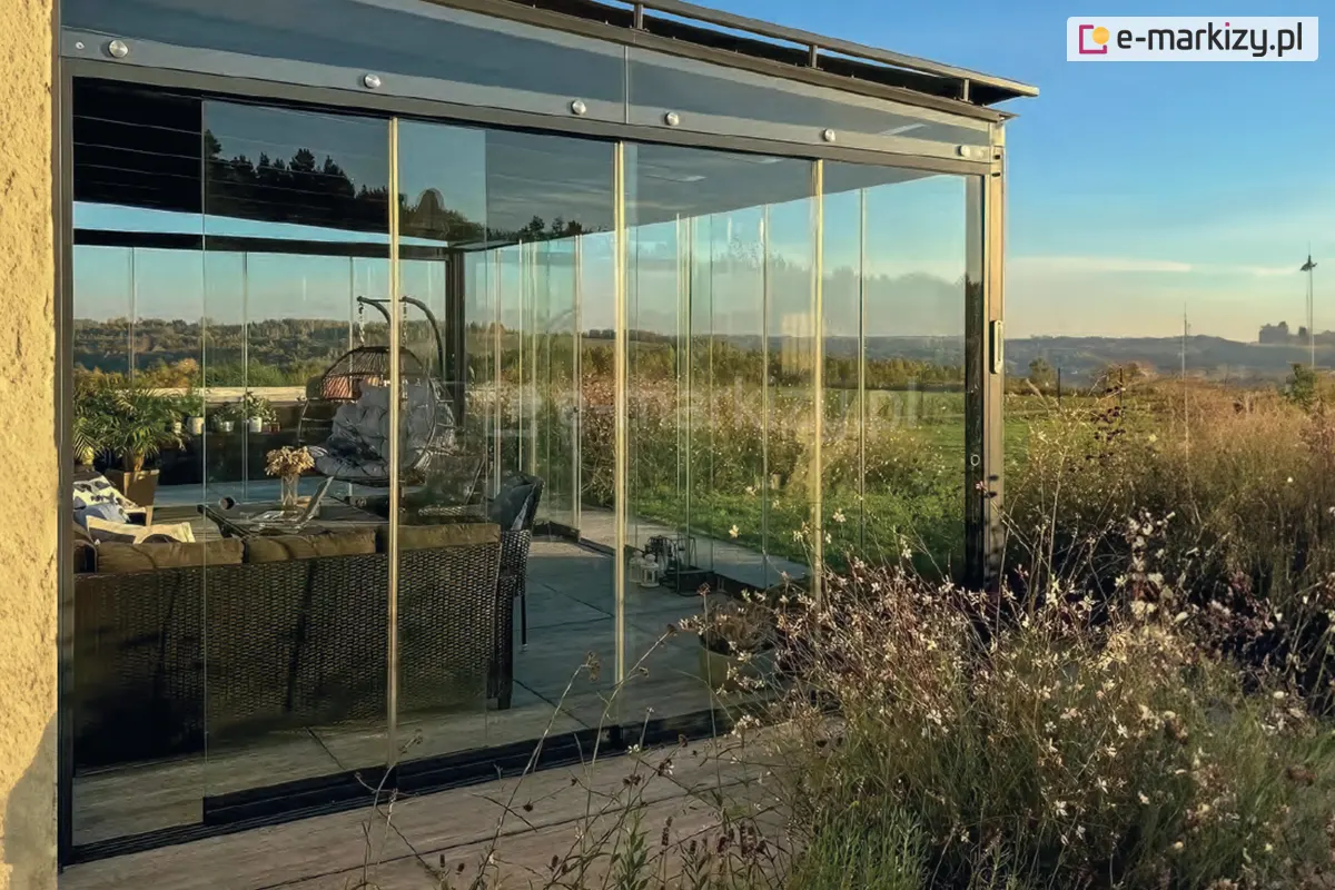 Szklana przybudowa domku z systemem drzwi przesuwnych Miros, tworząca osłoniętą strefę relaksu z panoramicznym widokiem na krajobraz i zachodzące słońce