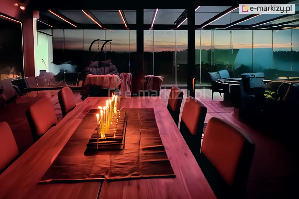 Nowoczesny ogród zimowy z przesuwnymi ścianami szklanymi Miros i nastrojowym oświetleniem LED, widoczny wieczorem przy zapalonych świecach