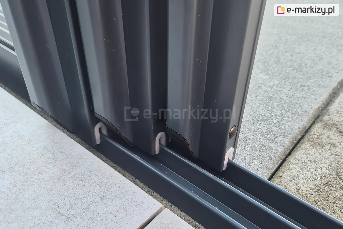 Zbliżenie na szyby zamontowane w przesuwnych panelach systemu Sotro, osadzonych w eleganckich, ciemnoszarych ramach aluminiowych. Panele płynnie przesuwają się na niezależnych torach prowadnicy.