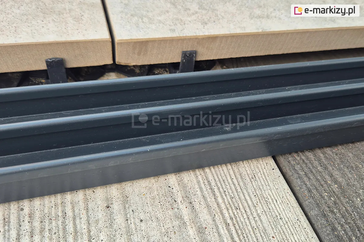 Zbliżenie na potrójne tory prowadzące do systemu szklanych drzwi przesuwnych Sotro, wykonane z solidnego, ciemnoszarego aluminium. Zdjęcie prezentuje precyzyjne wykończenie krawędzi po której poruszają się panele szklane.