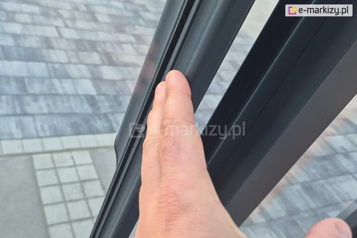 Zbliżenie na dłoń dotykającą ergonomiczny profil aluminiowy przesuwnych drzwi szklanych Sotro z eleganckim grafitowym obramowaniem