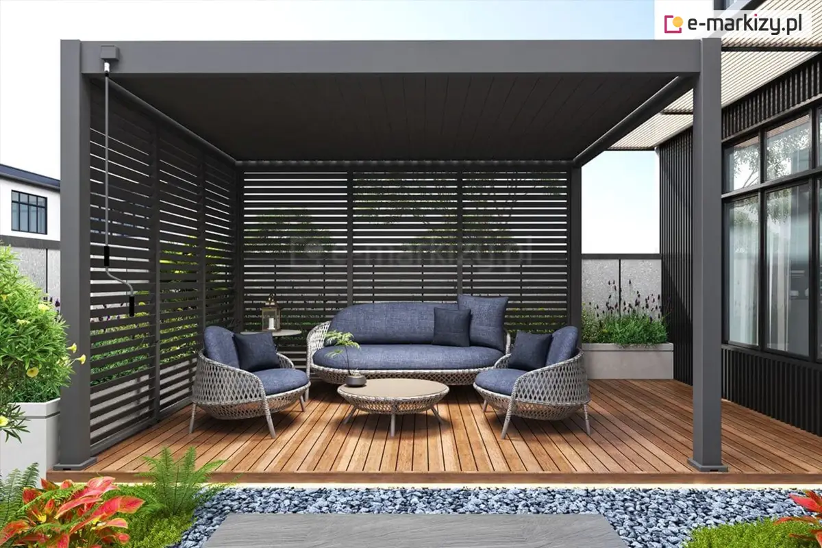 Aluminiowa pergola ogrodowa Marlo z bocznymi ściankami żaluzjowymi w kolorze antracytowym, tworząca elegancką i zaciszną strefę wypoczynkową na drewnianym tarasie. Wnętrze pergoli wyposażone w stylowe meble ogrodowe z niebieskimi poduszkami oraz okrągły stolik kawowy. Otoczenie pergoli zdobi bujna roślinność i starannie zaprojektowany ogród.