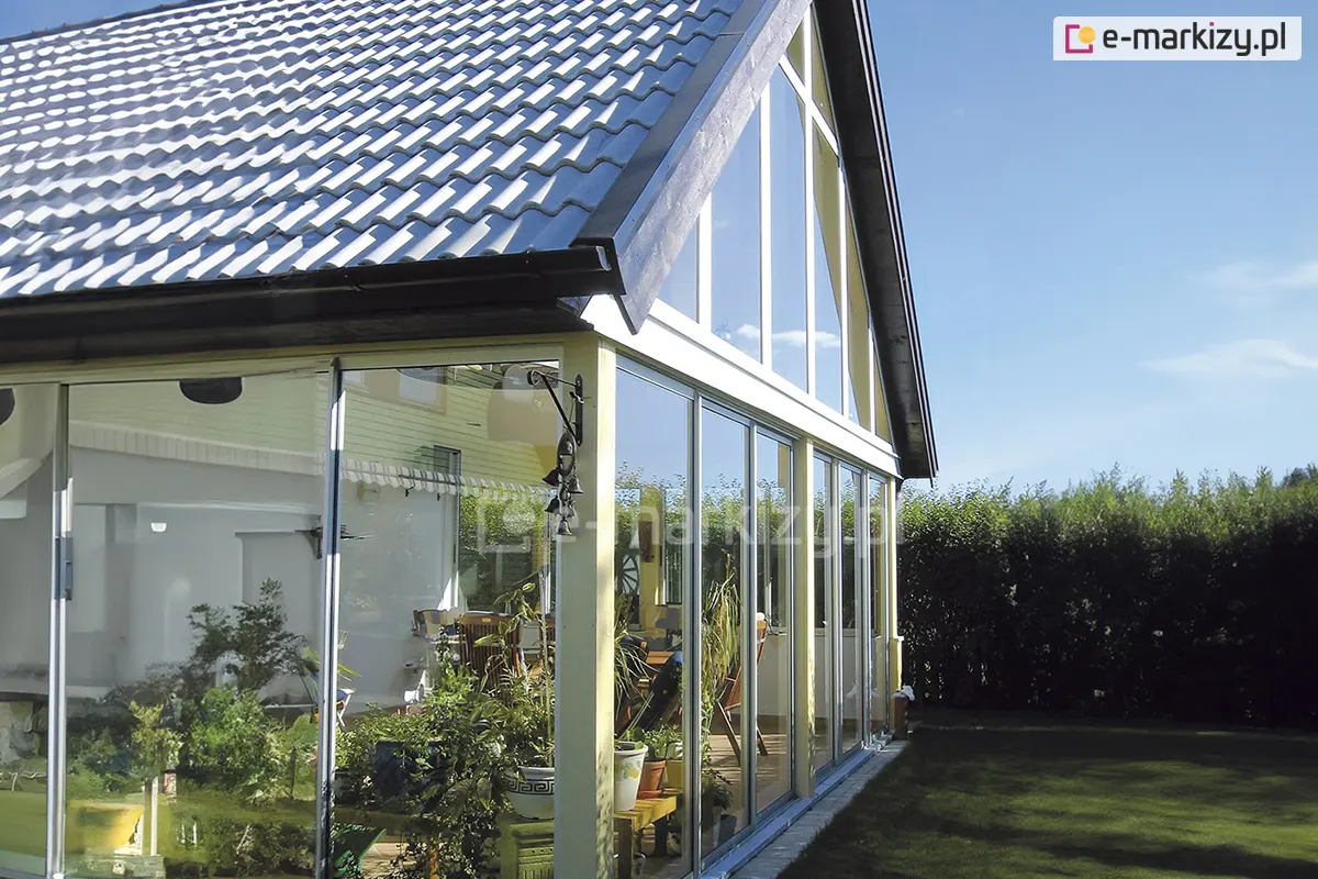 Szklana zabudowa ogrodu wykonana w systemie ramowym Sotro, z przesuwanymi drzwiami szklanymi i białą konstrukcją aluminiową, zamontowana przy domu jednorodzinnym z dwuspadowym dachem.