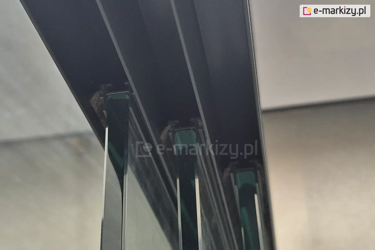 Zielonkawe panele szklane Miros na górnej prowadnicy trzytorowej, ukazujące detal montażu w zabudowie tarasowej z pergolą